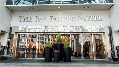 Front doors of the Pan Pacific Hotel Vancouver with four flower planters of different heights in the centre.